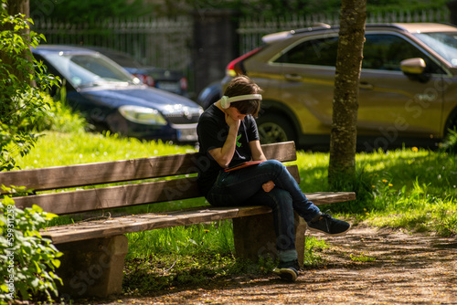 A young man relaxes in a park while looking at his tablet computer.