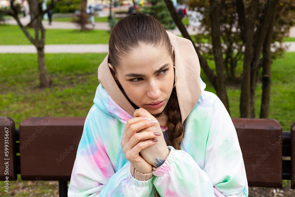 Portrait of a Young Slim brunette girl In the fitting clothes sitting on a bench outside on a beautiful spring day. Portrait of a Young Slim brunette girl In the fitting clothes sitting on a bench outside on a beautiful spring day.