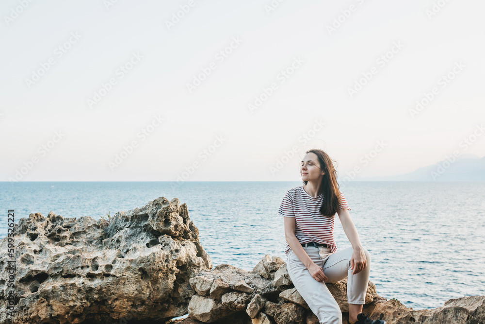 A young woman is sitting on the seashore and enjoying the sunset