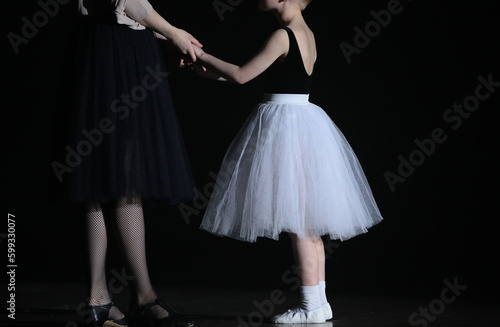 A young ballerina with a mentor studying in lesson standing in a black classroom holding hands