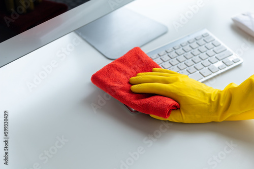 Person cleaning room, cleaning worker is using cloth to wipe computer keyboard in company office room. Cleaning staff. Concept of cleanliness in the organization.
