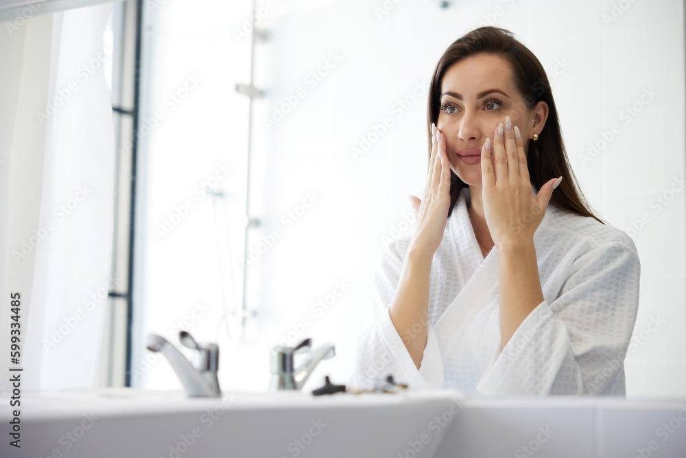 young woman looking at mirror and touching face in bathroom young woman looking at mirror and touching face in bathroom