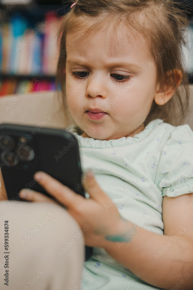 Adorable baby girl trying to use smartphone for watching cartoon. Baby and technology concept. Futuristic technology. Education internet technology. Playing Adorable baby girl trying to use smartphone for watching cartoon. Baby and technology concept. Futuristic technology. Education internet technology. Playing