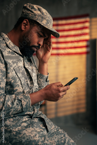 Worried soldier using cellphone indoors.
