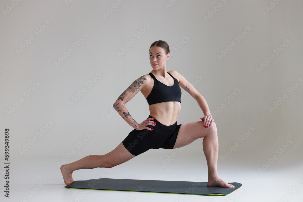 A young girl with brown hair, with a tattoo in a black top and shorts on a white background. Sports, fitness, stretching and yoga