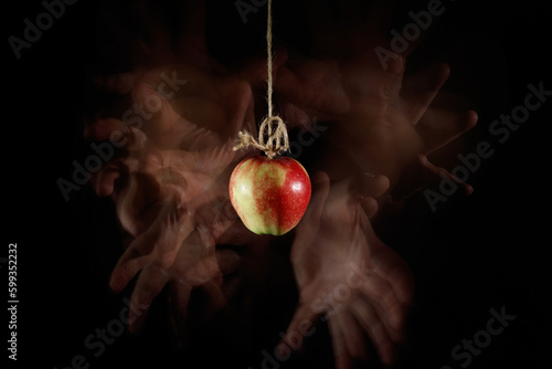 Wiszące na sznurku czerwone jabłko z chciwymi dłońmi wokół