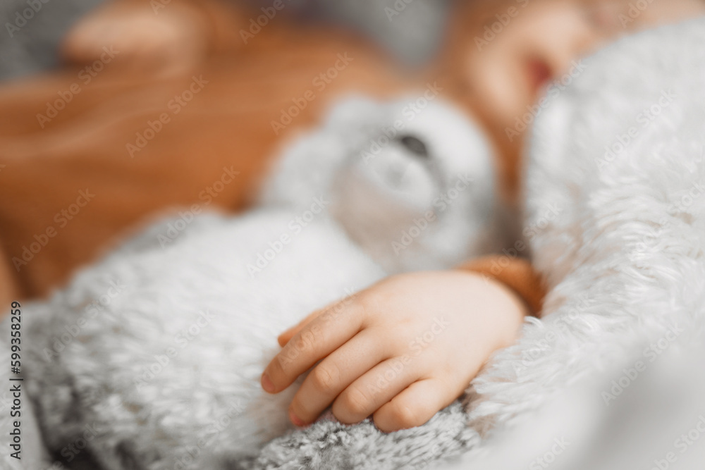 Close up hand of little baby lying in bed with fluffy stuffed toys of animals. Toddler sleeping with teddy bear in cozy room and enjoy healthy night sleep. Selective focus. Close up hand of little baby lying in bed with fluffy stuffed toys of animals. Toddler sleeping with teddy bear in cozy room and enjoy healthy night sleep. Selective focus.