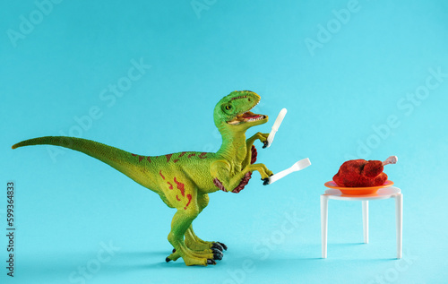 A cute little green dinosaur holds a fork and knife near a table with a roast turkey. © dvulikaia