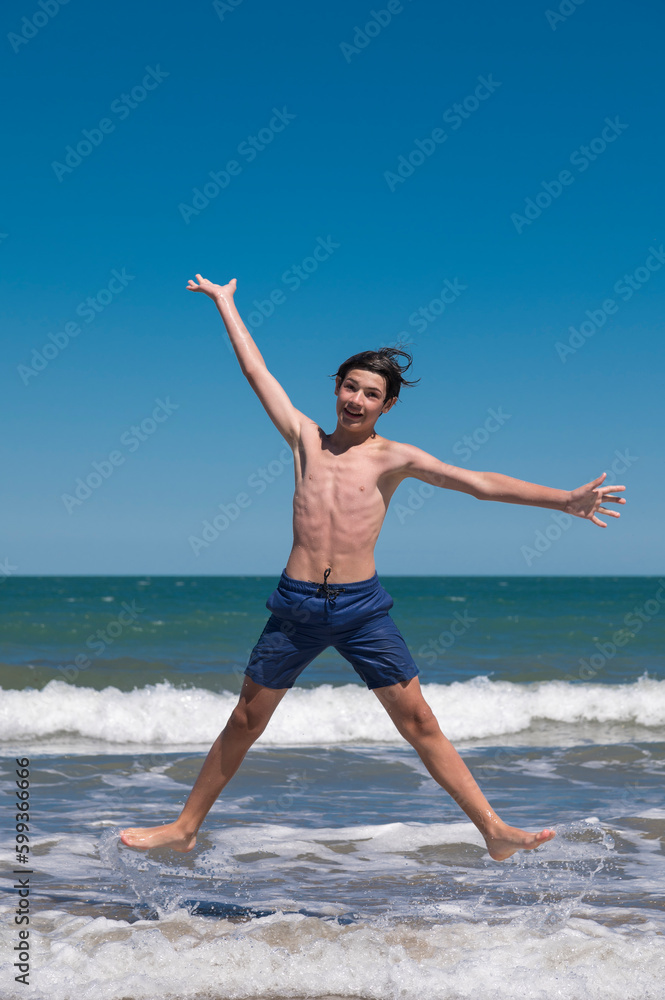 Happy boy performs pirouettes and big jumps on the seashore during his summer vacation on the Atlantic Coast, Las Grutas, Rio Negro, Argentina.