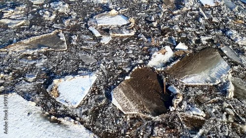 Handheld footage of dirty blocks of ice slowly floats down on the river.