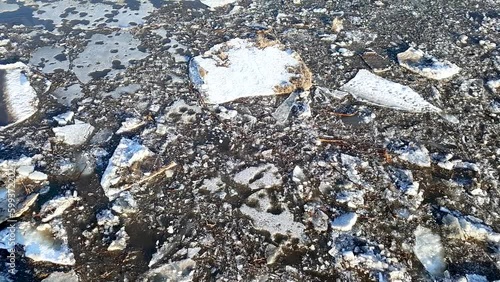 Handheld footage of dirty blocks of ice slowly floats down on muddy water.