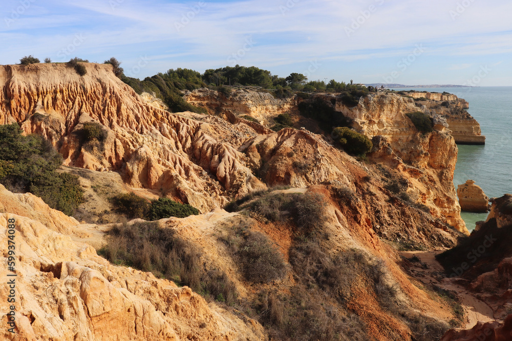 Orange limestone cliffs next to the Atlantic Ocean along the Seven Hanging Valleys hiking path in Algarve, Portugal.