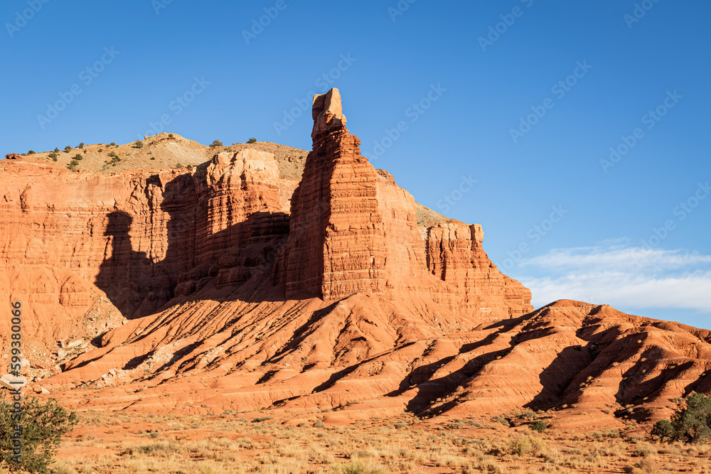 Fototapeta premium Red sandstone spire and mesa in a desert canyon in the desert landscape of Utahwith a cloudless blue sky.