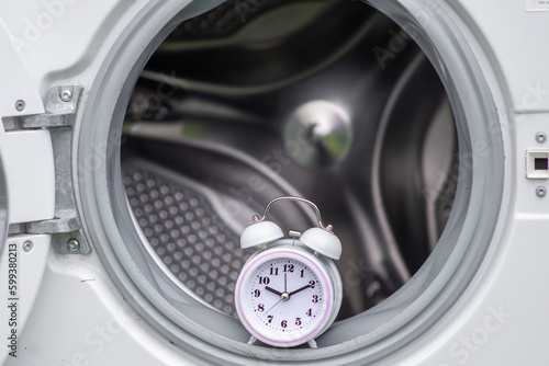 time and washing machine. Waiting, washing duration concept. Open door of washing machine and alarm clock. © Konstiantyn Zapylaie