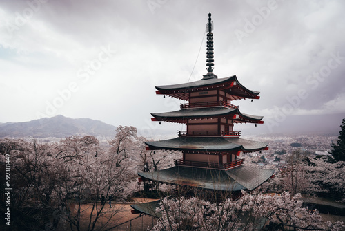 A pagoda towers over a traditional Japanese temple  surrounded by blossoming cherry trees and majestic mountains. The vibrant reds of the plants reflect centuries of faith  culture and history