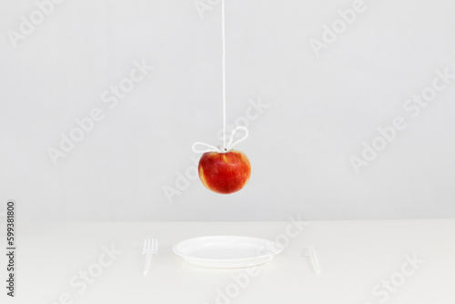 Wiszące na sznurku czerwone jabłko nad plastikowym jednorazowym talerzy ze sztućcami