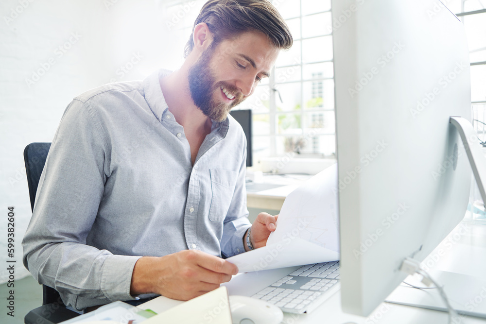 Action is the foundational key to success. a young designer holding paperwork while sitting in front of his computer. Action is the foundational key to success. a young designer holding paperwork while sitting in front of his computer.