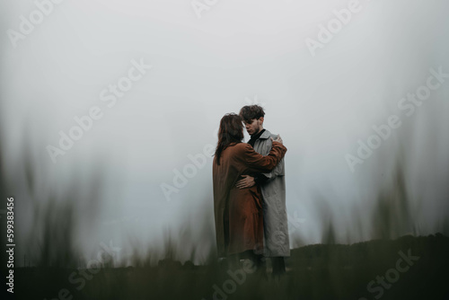 couple in love in raincoats in a foggy field embrace on a date. © velimir