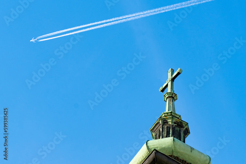 Baroque church tower with a green patina with a cross in the background with an airplane pulling a contrail