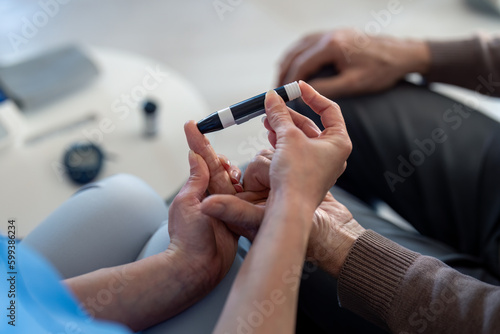 Close up photo of hands of a female doctor using lancet on finger to check patient's blood sugar level by glucose meter, poking male patient's finger with needle pen to measure blood sugar. photo