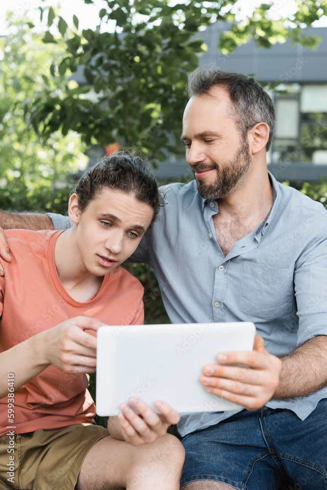 bearded dad looking at teenager son using digital tablet in green park. bearded dad looking at teenager son using digital tablet in green park.