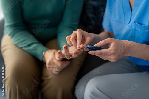 Unrecognizable female nurse measuring blood sugar during home visit. Caregiver using glucose meter device to check patient s blood sugar.