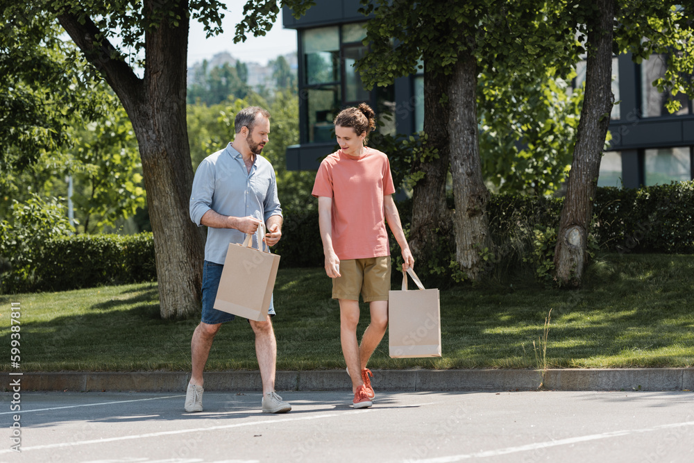 bearded father and teenage son walking with shopping bags outdoors.