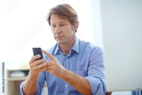 Im going to have to work a bit late tonight...a mature businessman reading a text message while sitting at his desk.