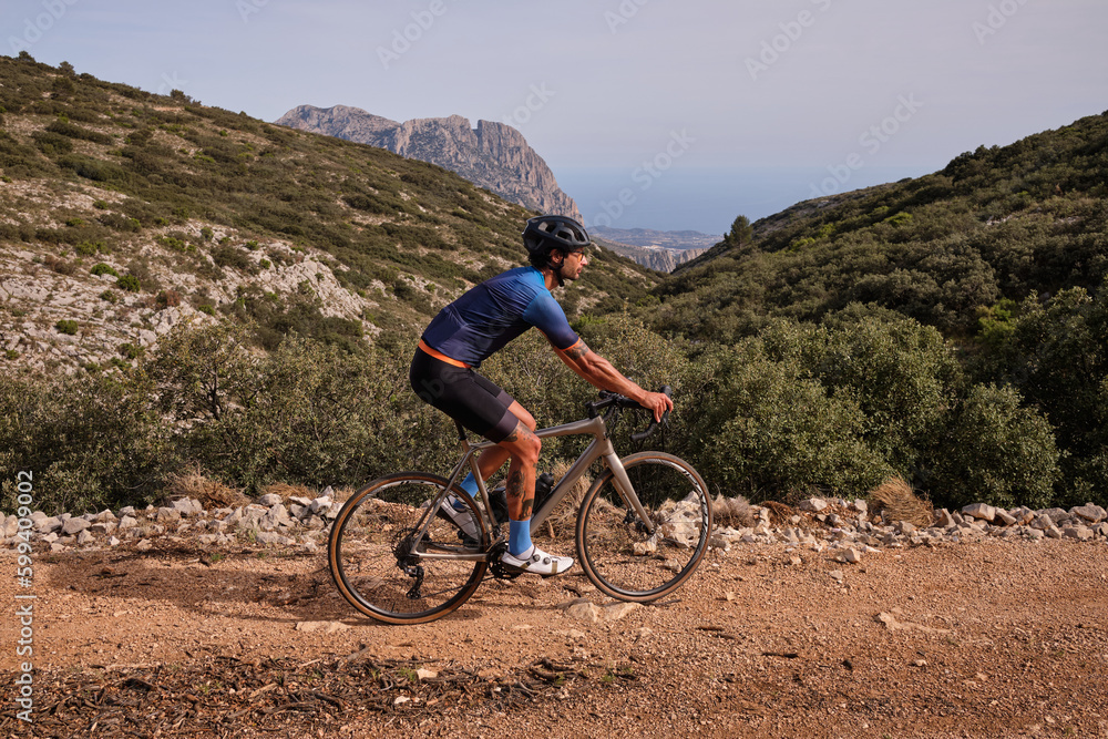 Fit male cyclist riding a gravel bike on a gravel road with a view of the mountains, Alicante region of Spain