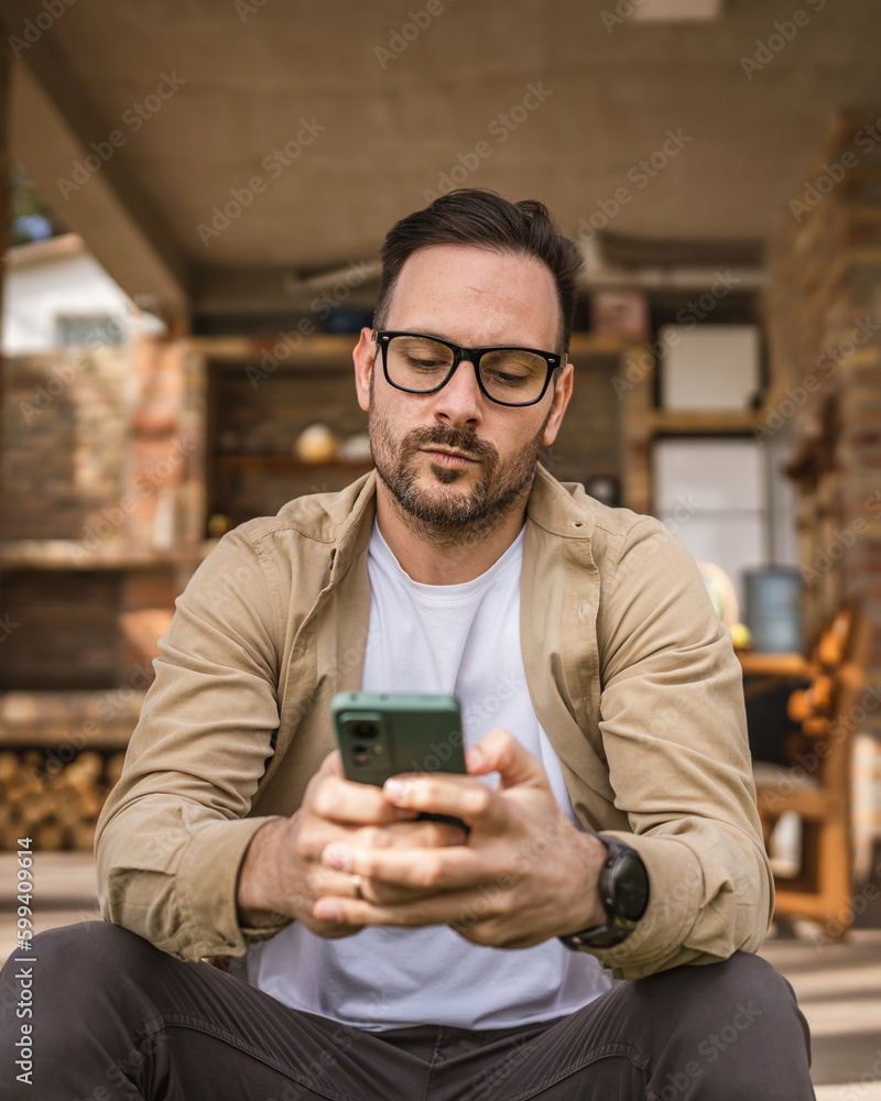Man Sitting in Front of House Use Smartphone and Look Worried Man Sitting in Front of House Use Smartphone and Look Worried