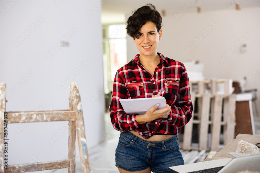 Fototapeta premium Positive latin woman construction manager checking project documentation while working in apartment.