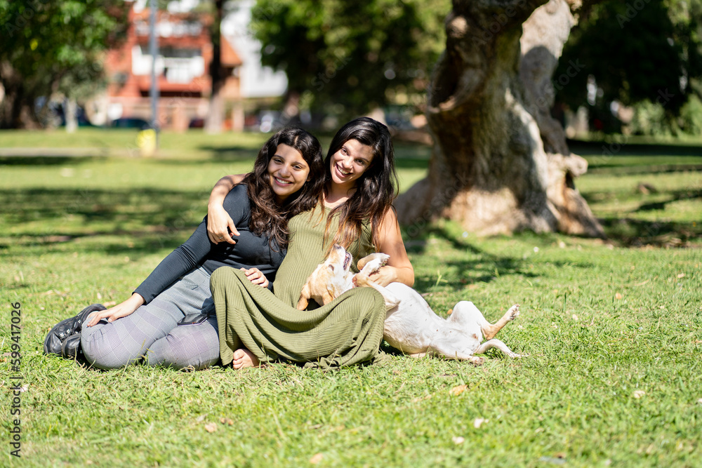 Pregnant latin woman sitting next to her daughter and dog posing looking at the camera with happy expression Pregnant latin woman sitting next to her daughter and dog posing looking at the camera with happy expression