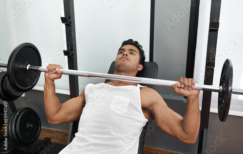 Bulking up his body. A young ethnic man lifting a heavy barbell.