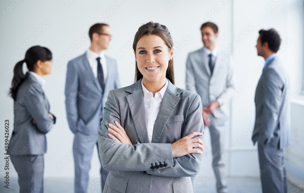 Confident in her business skills. A pretty young businesswoman smiling at you while her colleagues stand in the background. Confident in her business skills. A pretty young businesswoman smiling at you while her colleagues stand in the background.