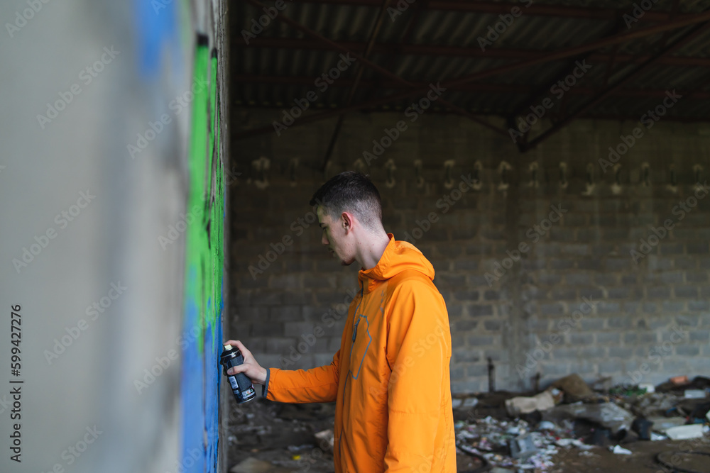 One young guy drawing graffiti on wall with spray can and mask on his face during the day One young guy drawing graffiti on wall with spray can and mask on his face during the day