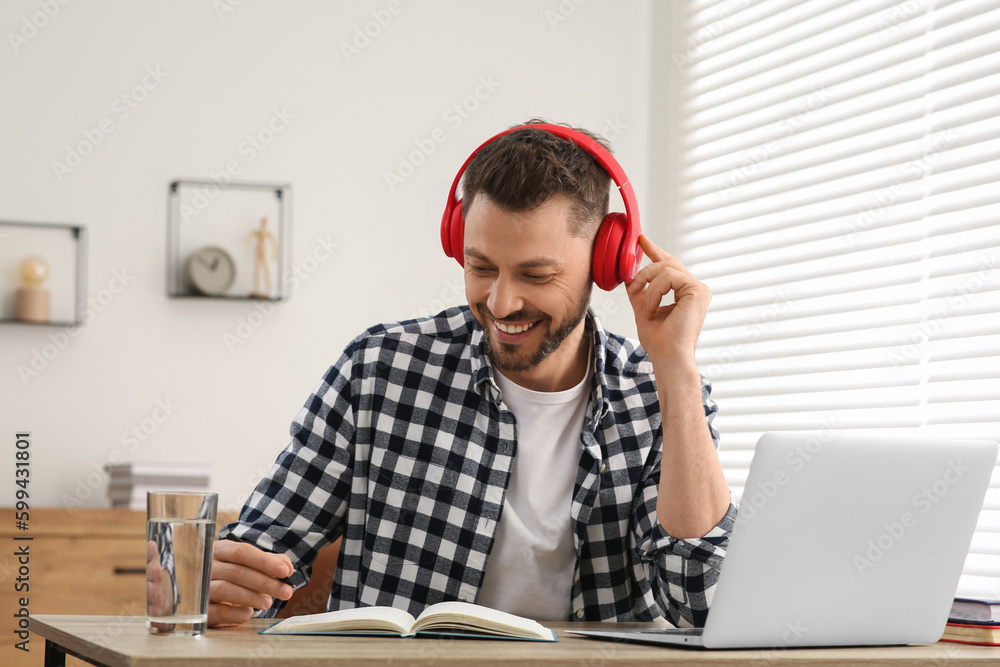 Naklejka premium Man in headphones studying on laptop at home. Online translation course