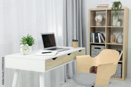 Workplace with modern laptop on desk and comfortable chair at home