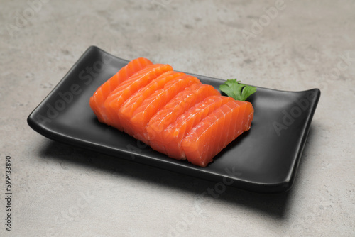 Plate of tasty salmon slices and parsley on grey table. Delicious sashimi dish