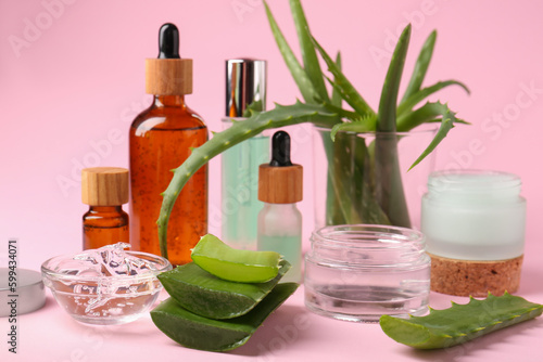 Cosmetic products and cut aloe on pink background