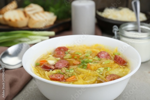 Delicious sauerkraut soup with smoked sausages and green onion on table, closeup