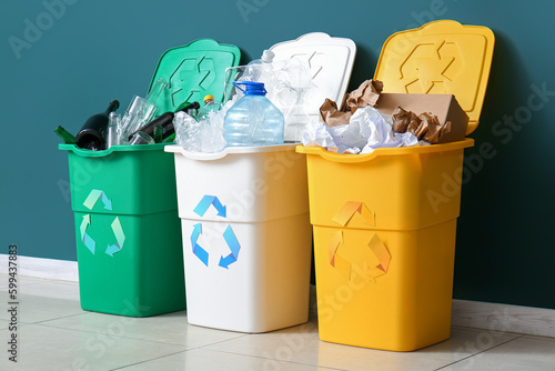 Trash bins with recycling symbol and different garbage near green wall