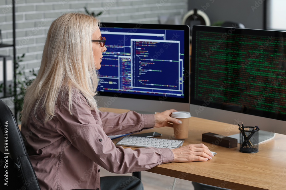 Mature female programmer working with computer at table in office Mature female programmer working with computer at table in office