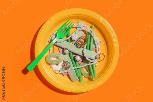 Plate with jelly candies and jewelry on color background