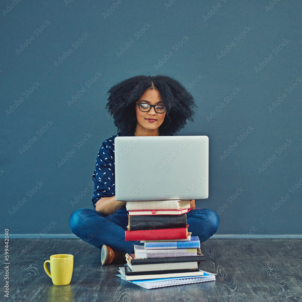 A grades only for her. Studio shot of a young woman using a laptop with books stacked in front of her against a gray background. A grades only for her. Studio shot of a young woman using a laptop with books stacked in front of her against a gray background.