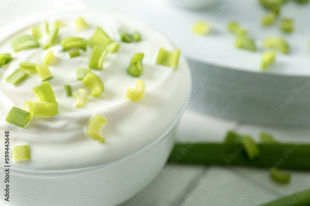 Bowl with sour cream and sliced green onion on white tile table Bowl with sour cream and sliced green onion on white tile table