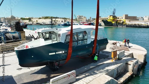 Drone aerial shot flying towards a boat lifted in air while workmen are checking lifting straps around it at MMH ship yard Malta photo