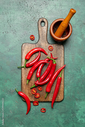 Wooden board with fresh chili peppers on green background