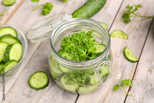 Jar with pieces of fresh cucumber on light wooden background
