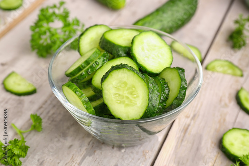 bowl with pieces of fresh cucumber on light wooden background