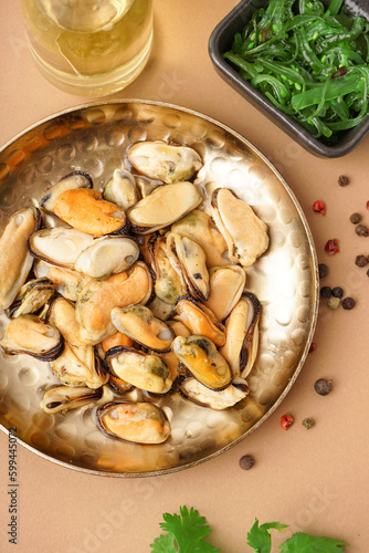 Plate with pickled mussels and bowl of seaweed salad on brown background